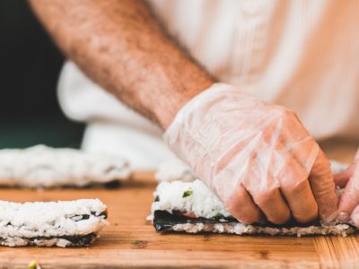 A hand in a white glove rolling sushi at a sushi making class.