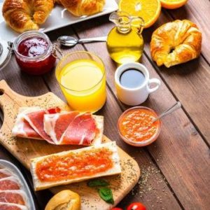 Spanish tomato and ham toast, croissant, coffee, orange juice. Traditional Mediterranean breakfast or lunch on wooden table. The composition is at the left of an horizontal frame leaving useful copy space for text and/or logo at the right. High angle view. High resolution 42Mp studio digital capture taken with SONY A7rII and Zeiss Batis 40mm F2.0 CF lens