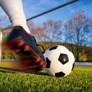 Football or soccer shot with a neutral design ball being kicked, with motion blur on the foot and natural background