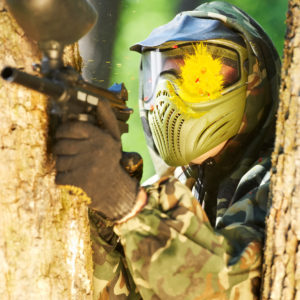 paintball sport player wearing protective mask aiming gun with head shot by paint spot