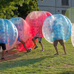 Teenagers play in Bubble bump, new and fun team game outdoor. Children are inside of blown plastic transparent bubble shock each other with fun. Out of focus park zone is at background