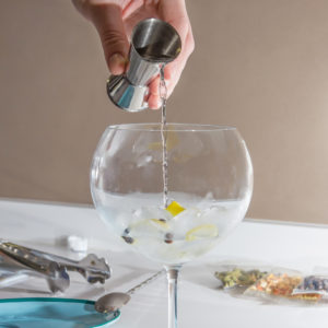 Closeup of barman hand pouring alcoholic drink with a jigger on glass to prepare gin tonic cocktail