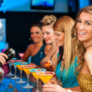 Young people in club or bar drinking cocktails and having fun; the barkeeper is mixing drinks