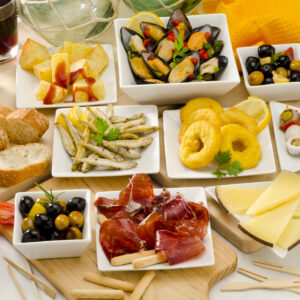 Spanish cuisine. Assortment of Tapas including Serrano Ham, Manchego Cheese, Marinated Olives, Pikles, Potatoes in Hot Sauce, and others, served with red wine.