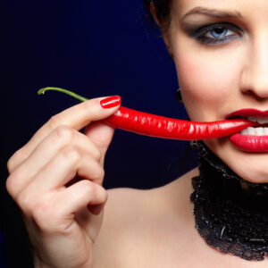 portrait of beautiful brunette girl in black lacy collar biting spicy hot red cayenne chilli pepper